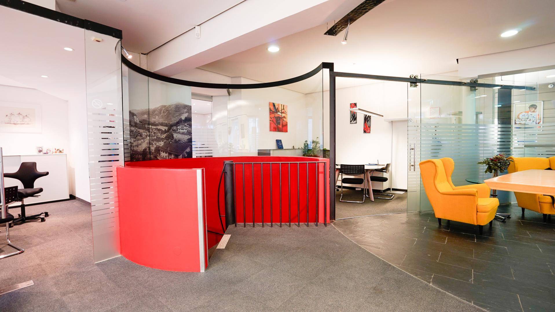 Büro-Empfangsbereich mit roten Theken, gelben Sitzgelegenheiten und transparenten Glaswänden.