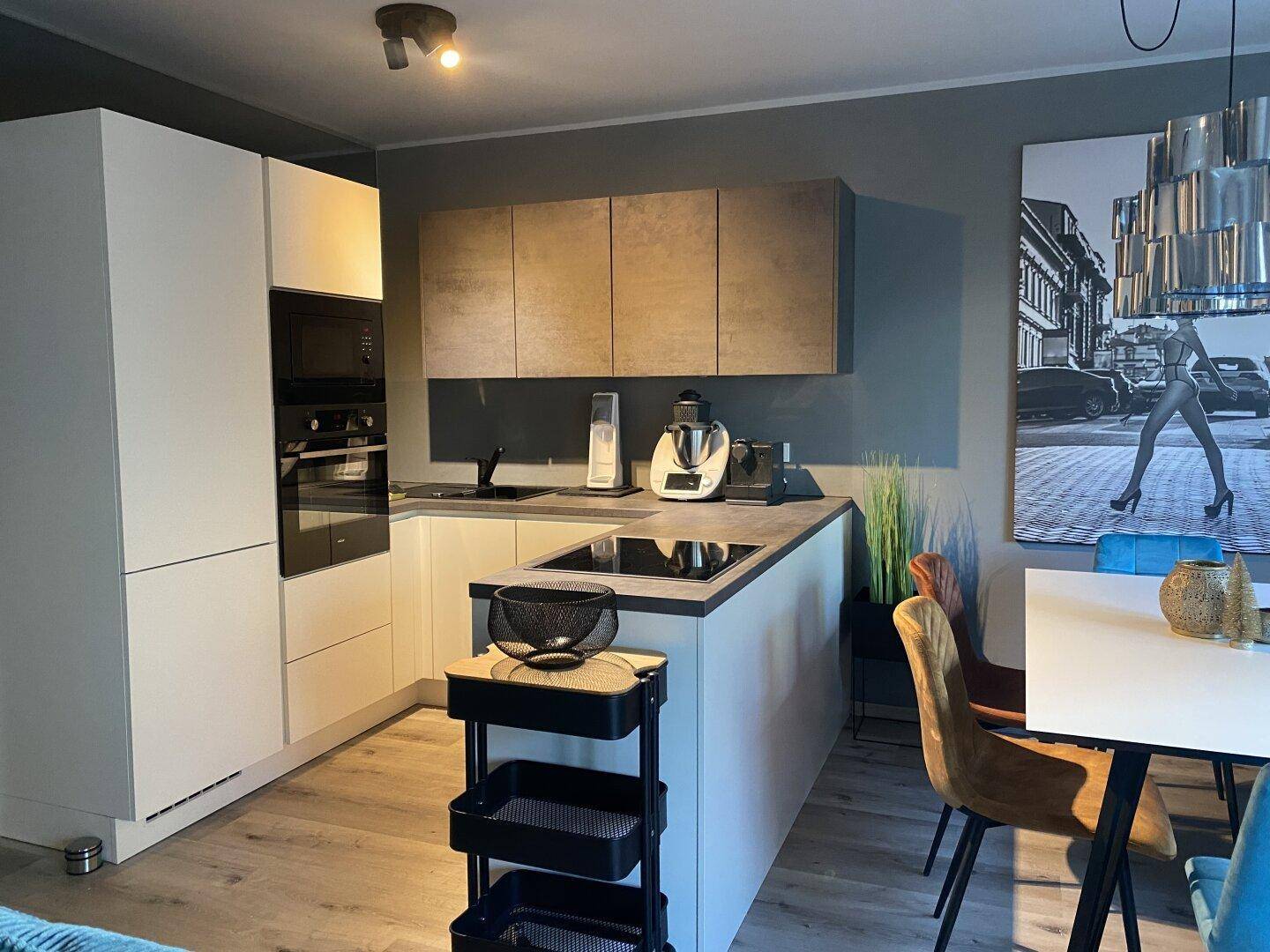 Moderne Einbauküche mit Kochinsel, integrierten Geräten und stilvoller Beleuchtung.