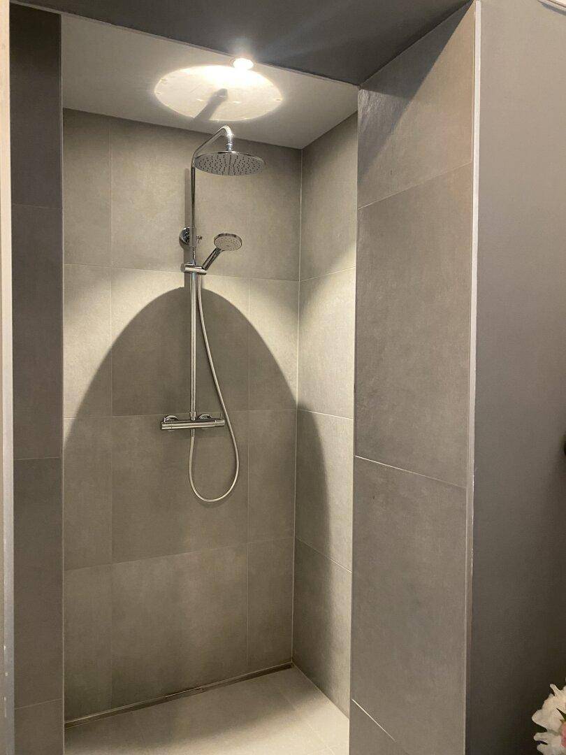 Geräumige, ebenerdige Dusche mit Regenduschkopf und modernen grauen Fliesen.