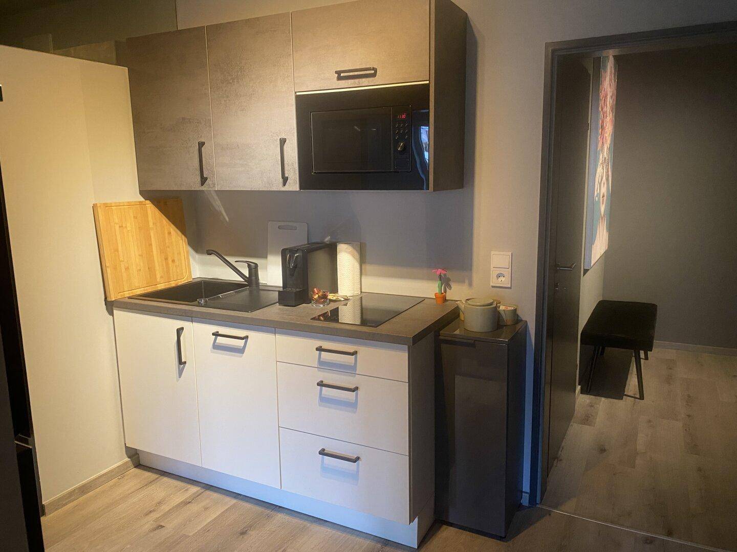 Kompakte Küchenzeile mit Mikrowelle, Kochfeld und Spüle, ideal für kleine Wohnungen.