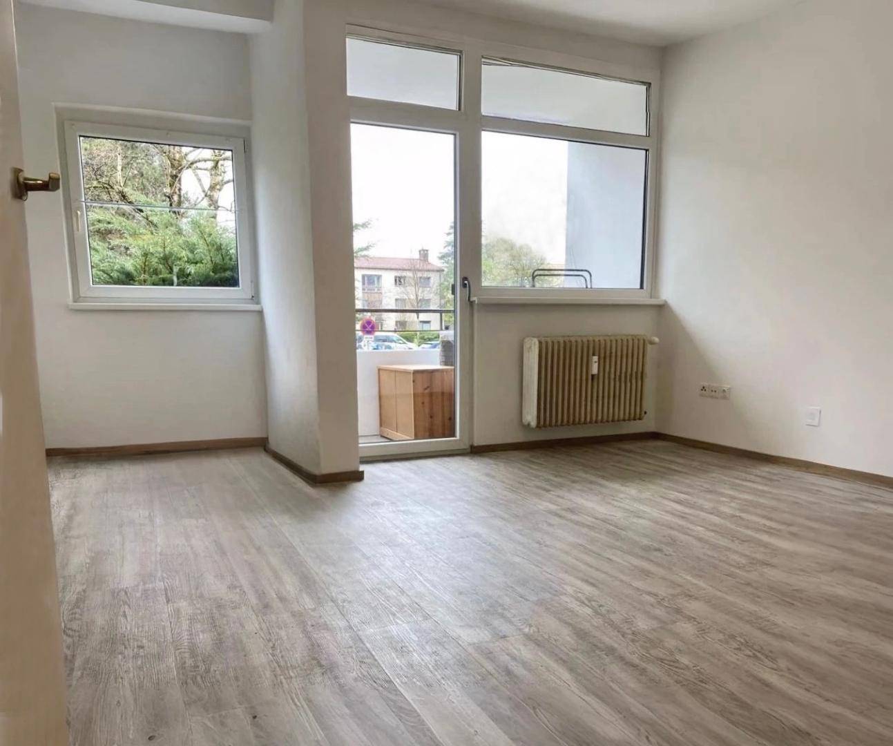 Heller Wohnraum mit Laminatboden, großen Fenstern und direktem Zugang zu einem Außenbereich.