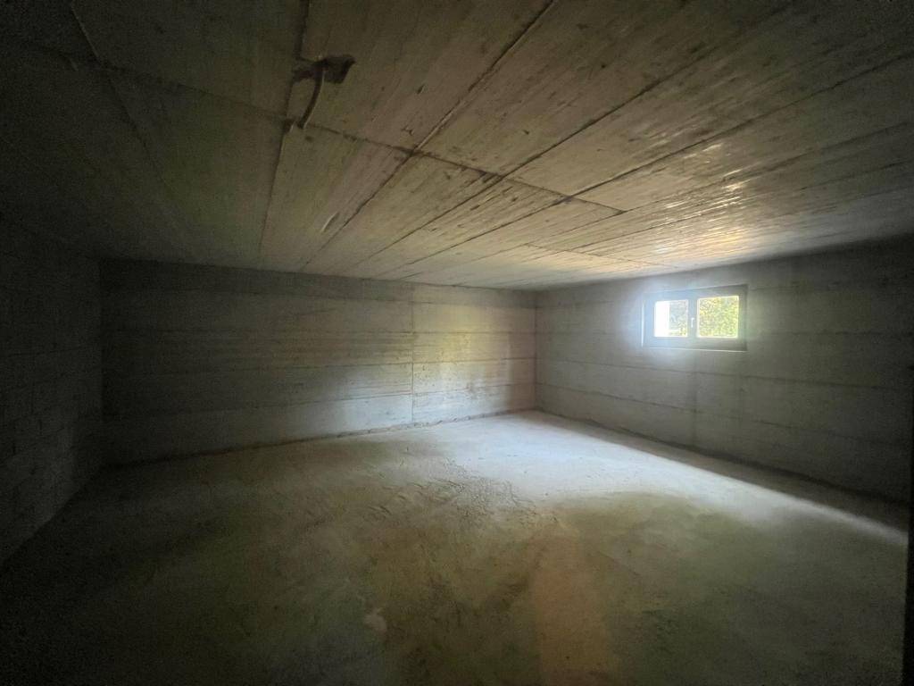 Dunkler Kellerraum mit Betonwänden und einem kleinen Fenster, bietet Stauraum.
