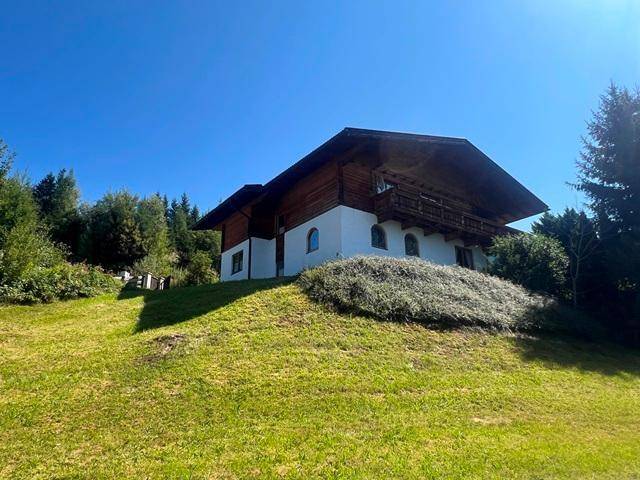 Traditionelles Haus auf einem Hügel mit Holzbalkonen, umgeben von Bäumen und grüner Landschaft.