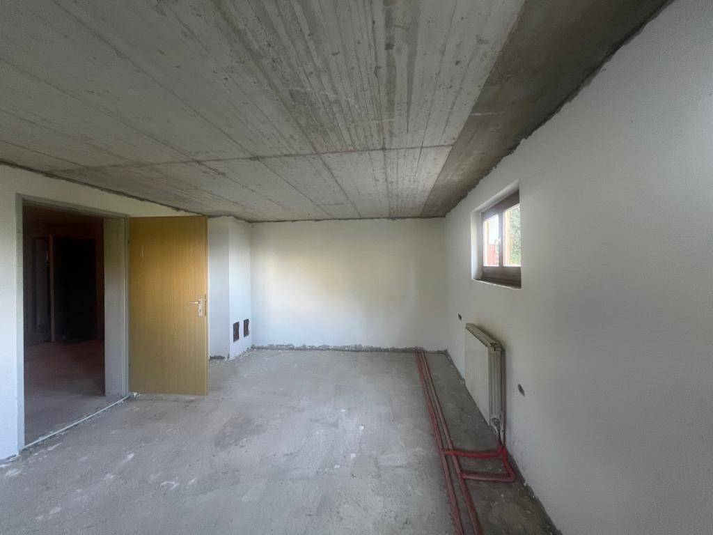 Unfertiger Raum mit Betonboden und einem Fenster, ideal für zukünftige Nutzung.