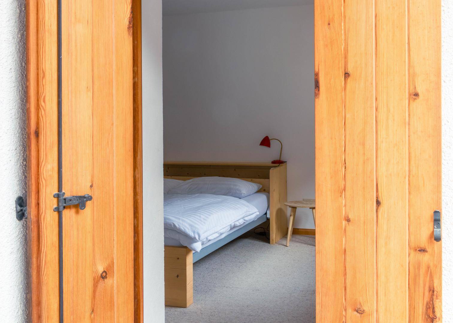 Blick in ein helles Schlafzimmer durch offene Holzschiebetüren mit einem gemütlichen Bett.