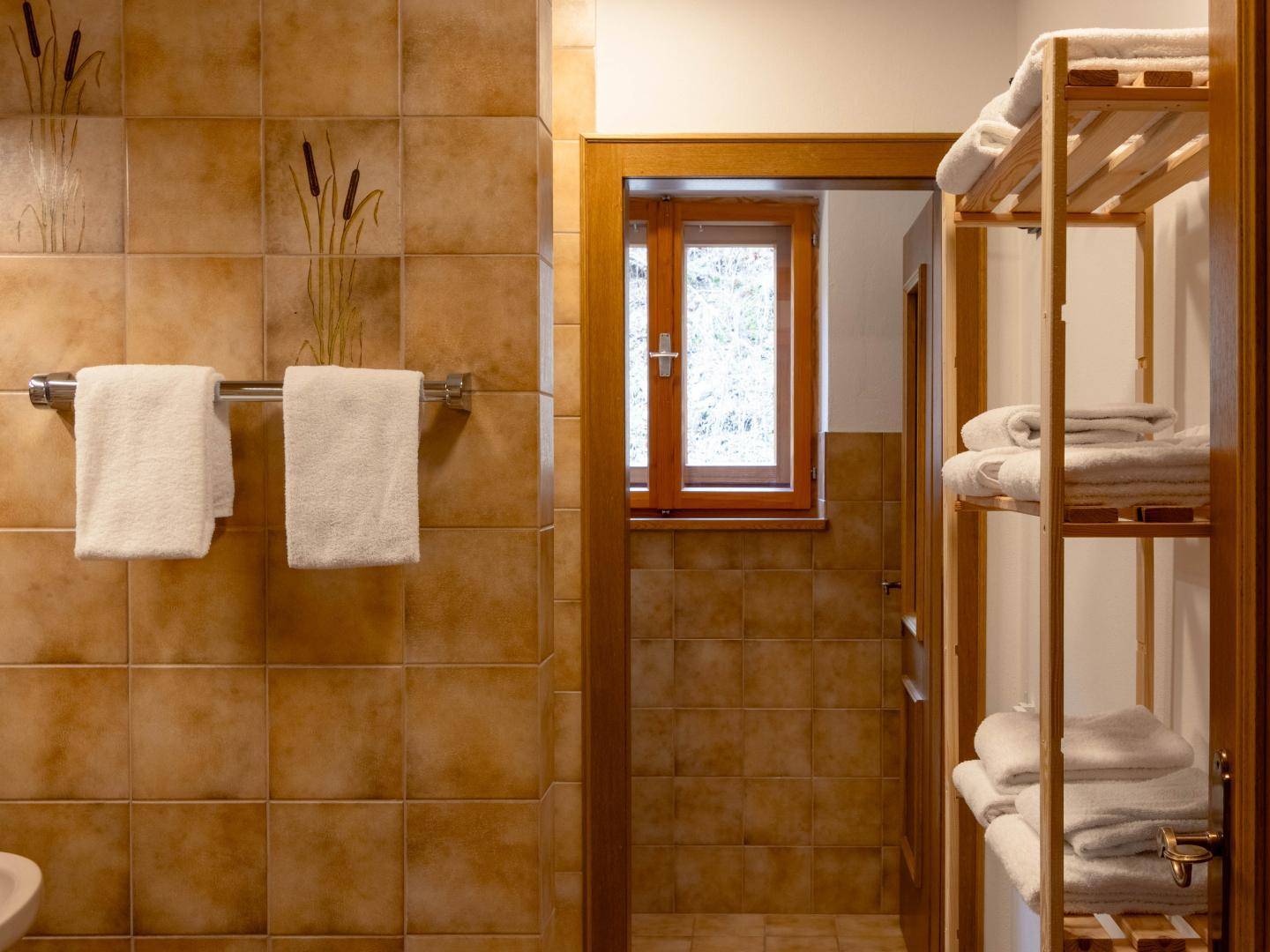 Badezimmer mit braunen Fliesen, Handtuchhalter und Holzregal, ausgestattet mit einem Fenster.