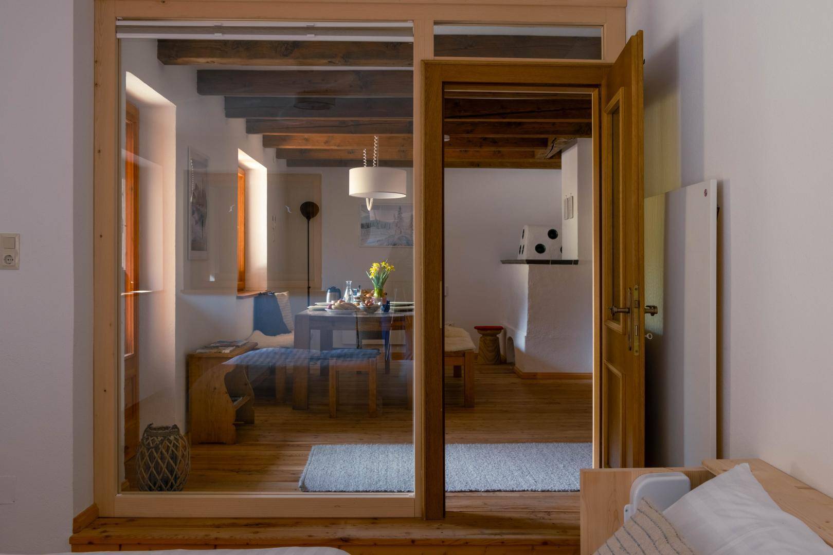 Gemütliches Schlafzimmer mit Blick durch eine Glastür in einen Essbereich mit Holzbalken.