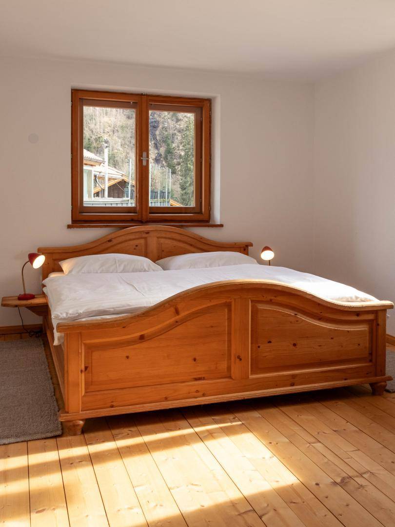Gemütliches Schlafzimmer mit traditionellem Holzbett, weißer Bettwäsche und Fensterblick.
