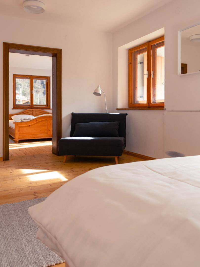 Helles Schlafzimmer mit Holzboden, gemütlichem Sessel und Zugang zu einem weiteren Schlafzimmer.
