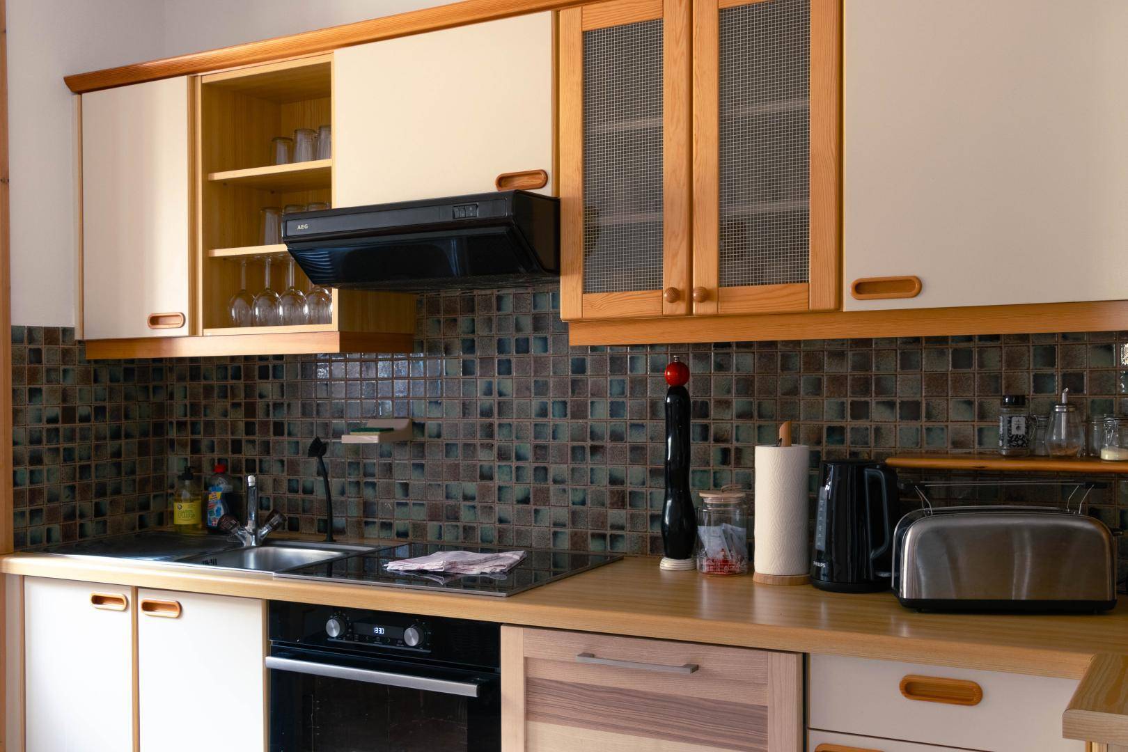 Funktionale Küche mit Holzschränken, gemusterten Fliesen und integrierten Elektrogeräten.
