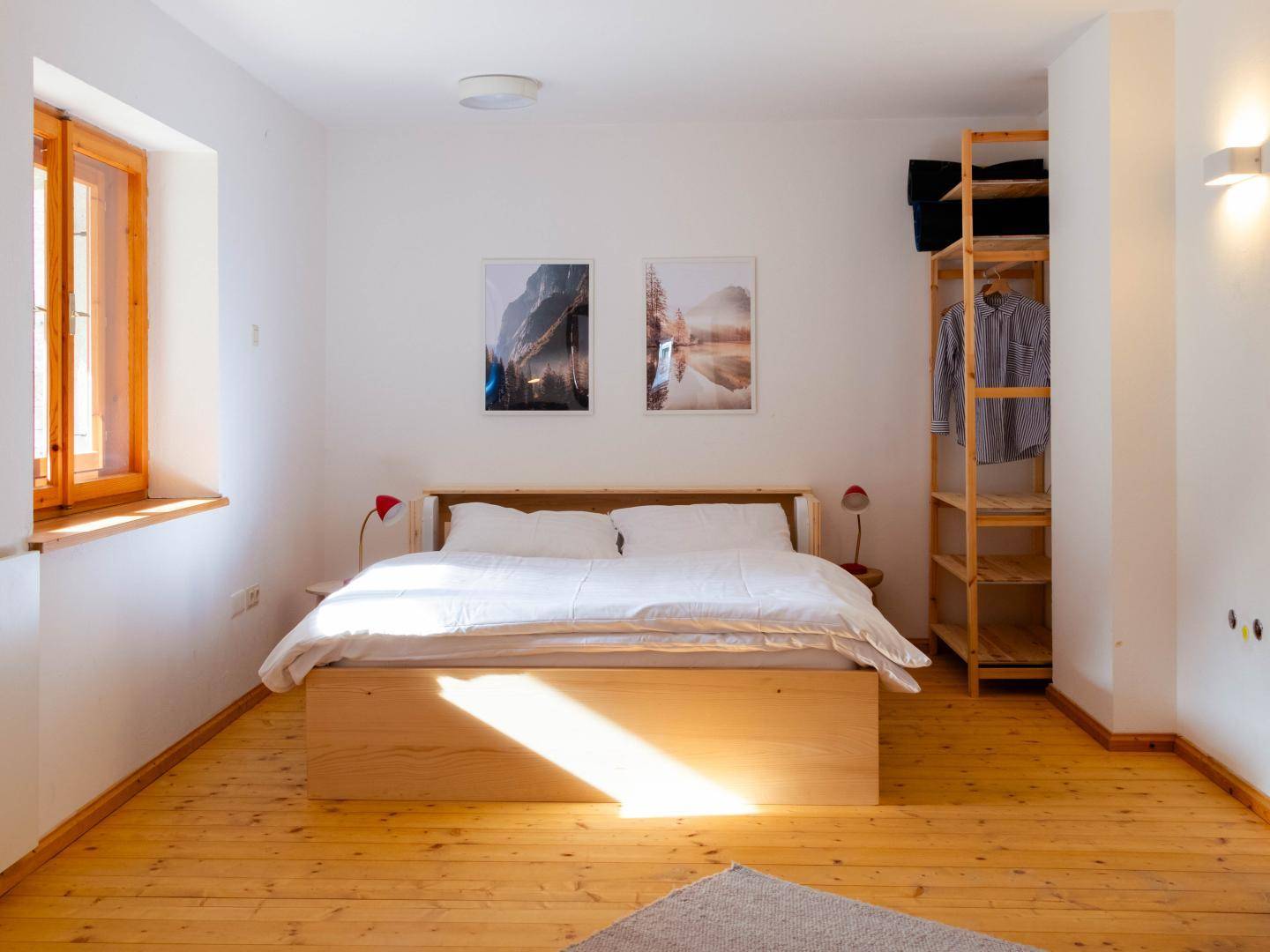 Geräumiges Schlafzimmer mit Holzbett, Holzboden und zwei Bildern an der weißen Wand.