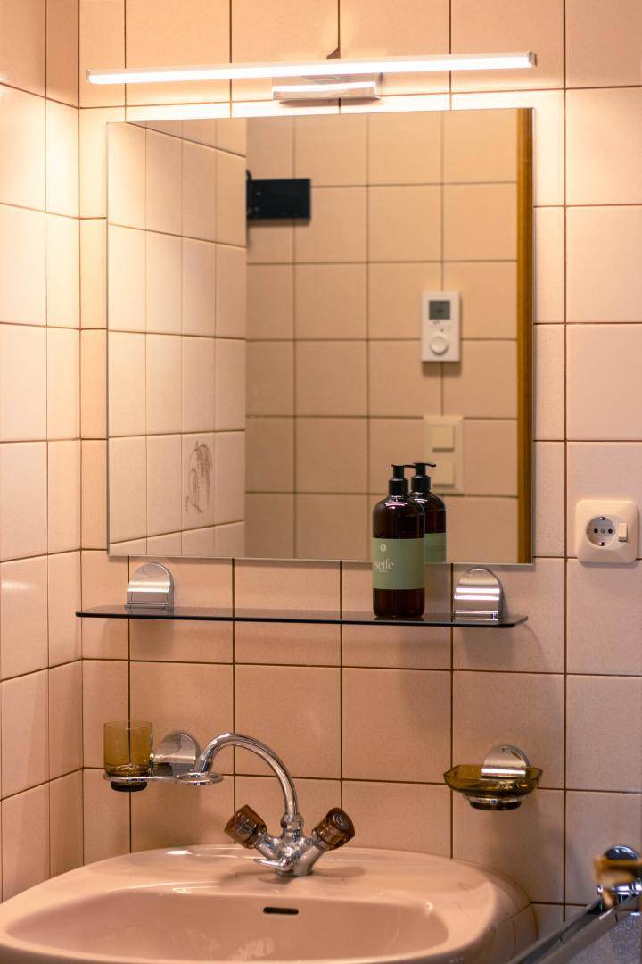Badezimmer mit beigen Fliesen, Einzelwaschbecken und einem beleuchteten Spiegelschrank.