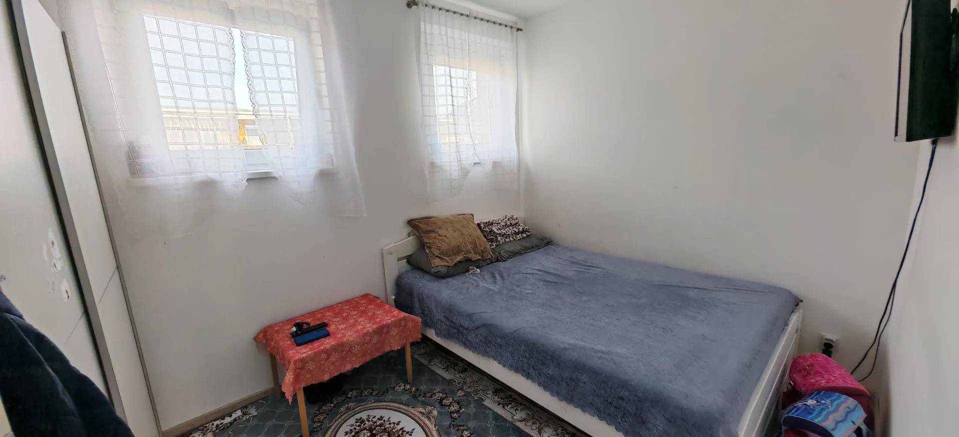 Kleines Schlafzimmer mit Einzelbett, zwei Fenstern und Laminatboden.