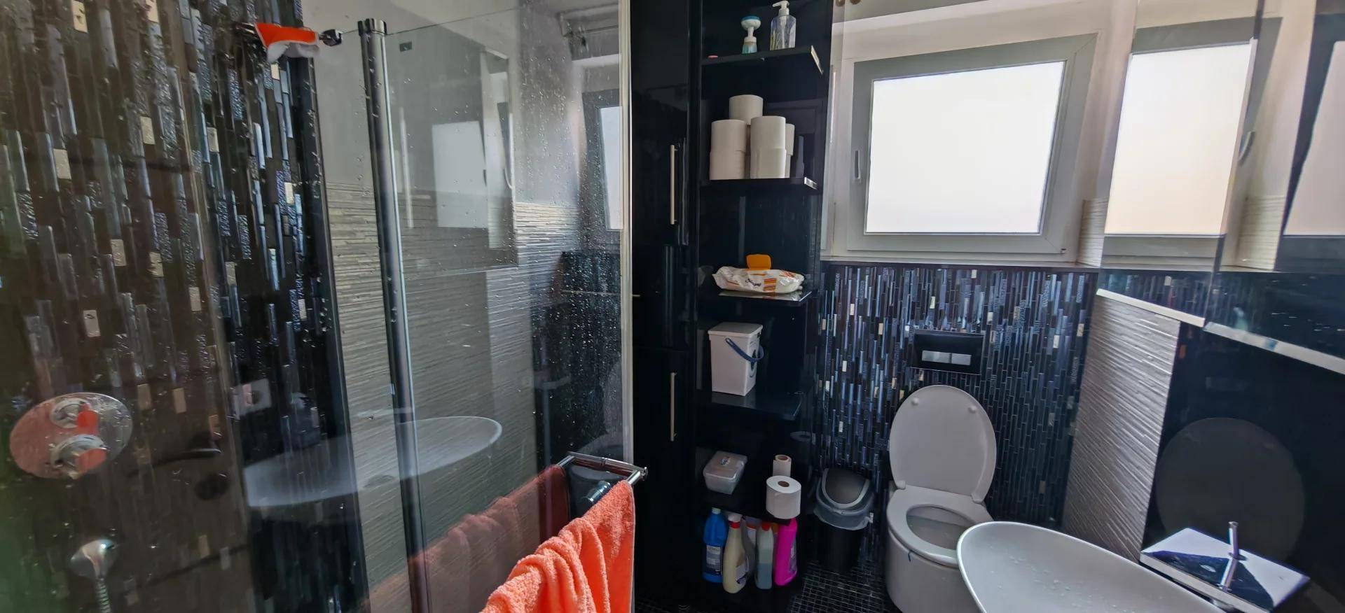 Modernes Badezimmer mit dunklen Fliesen, Duschkabine und Fenster.