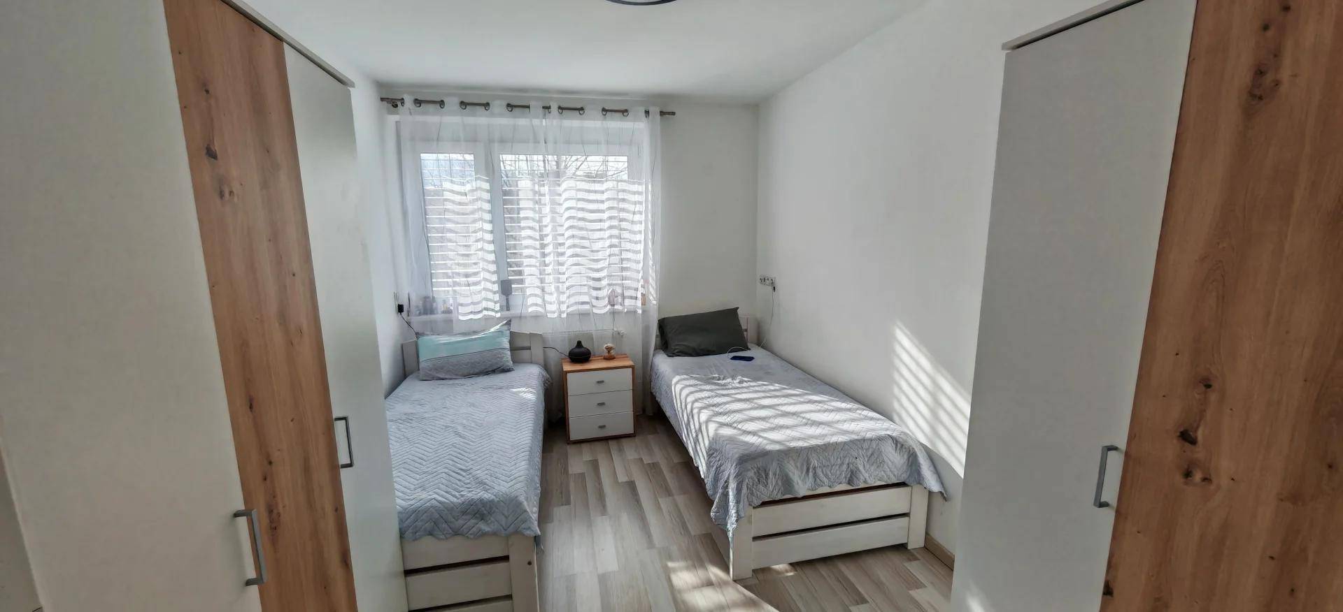 Helles Schlafzimmer mit zwei Einzelbetten, Holzboden und großem Fenster.