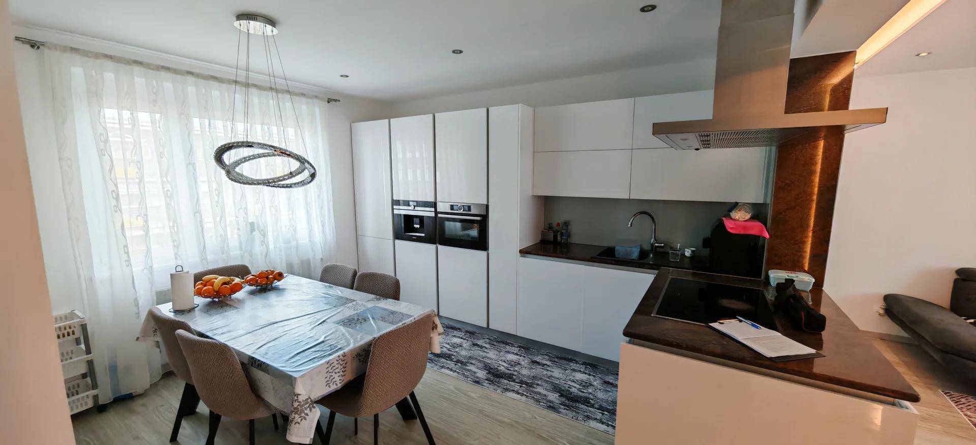 Helle, moderne Küche mit weißen Schränken, integrierten Geräten und Esstisch am Fenster.