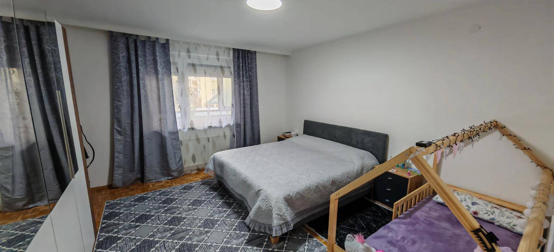 Helles Schlafzimmer mit Doppelbett, Kinderbett und Teppichboden, ideal für Familien.