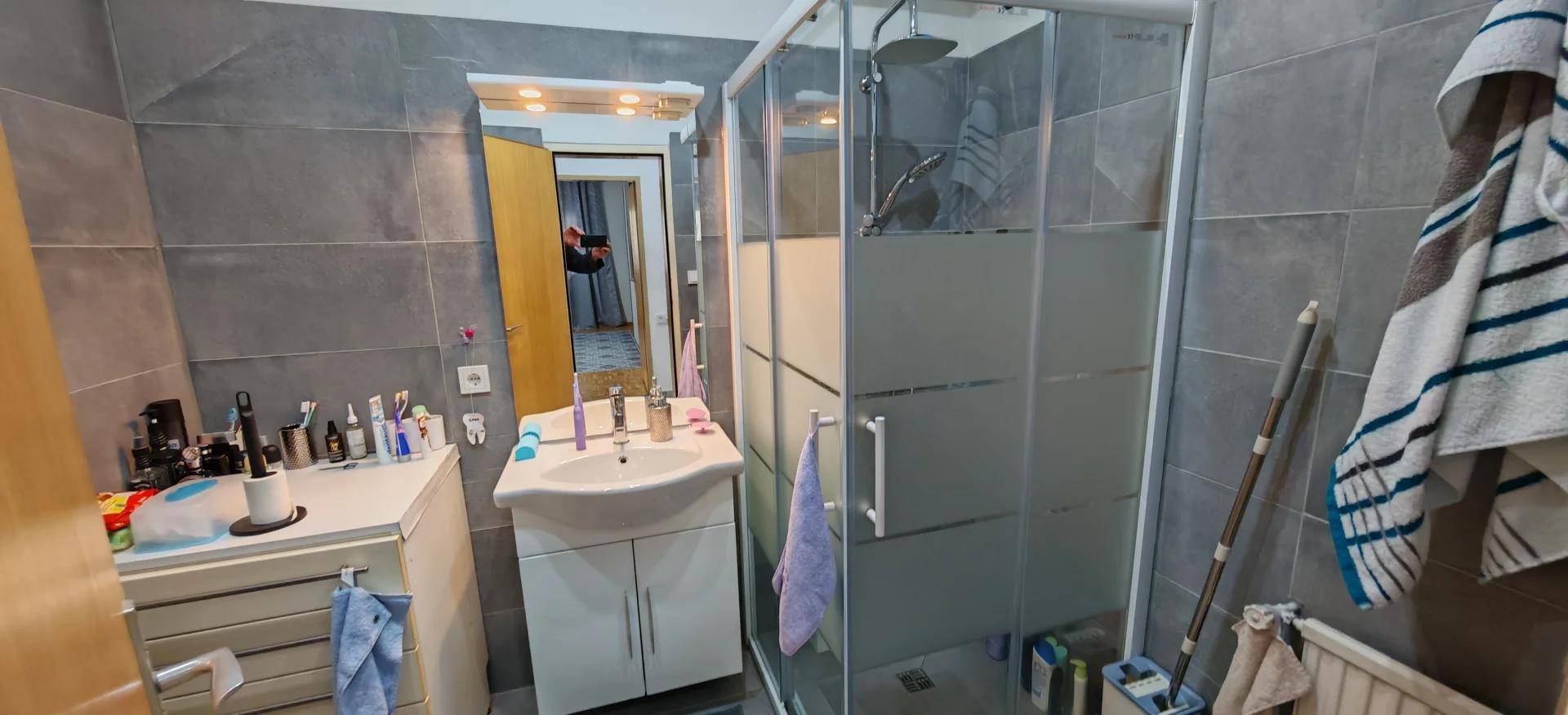 Modernes Badezimmer mit grauen Fliesen, Duschkabine und Einzelwaschbecken.