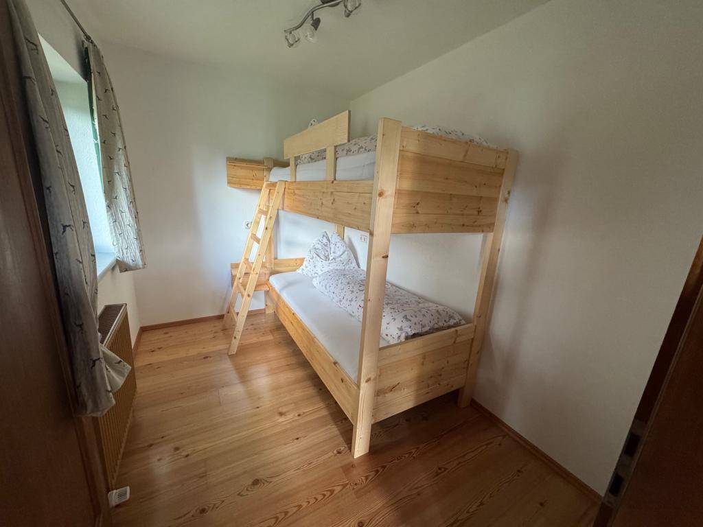 Helles Schlafzimmer mit Etagenbett aus Holz, Holzboden und einem Fenster mit Blick ins Grüne.