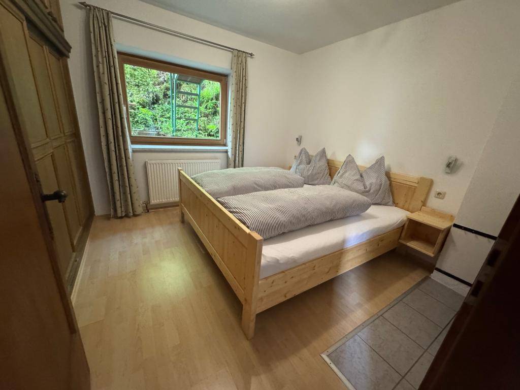 Gemütliches Schlafzimmer mit Doppelbett, Holzboden und einem Fenster, das viel Tageslicht hereinlässt.