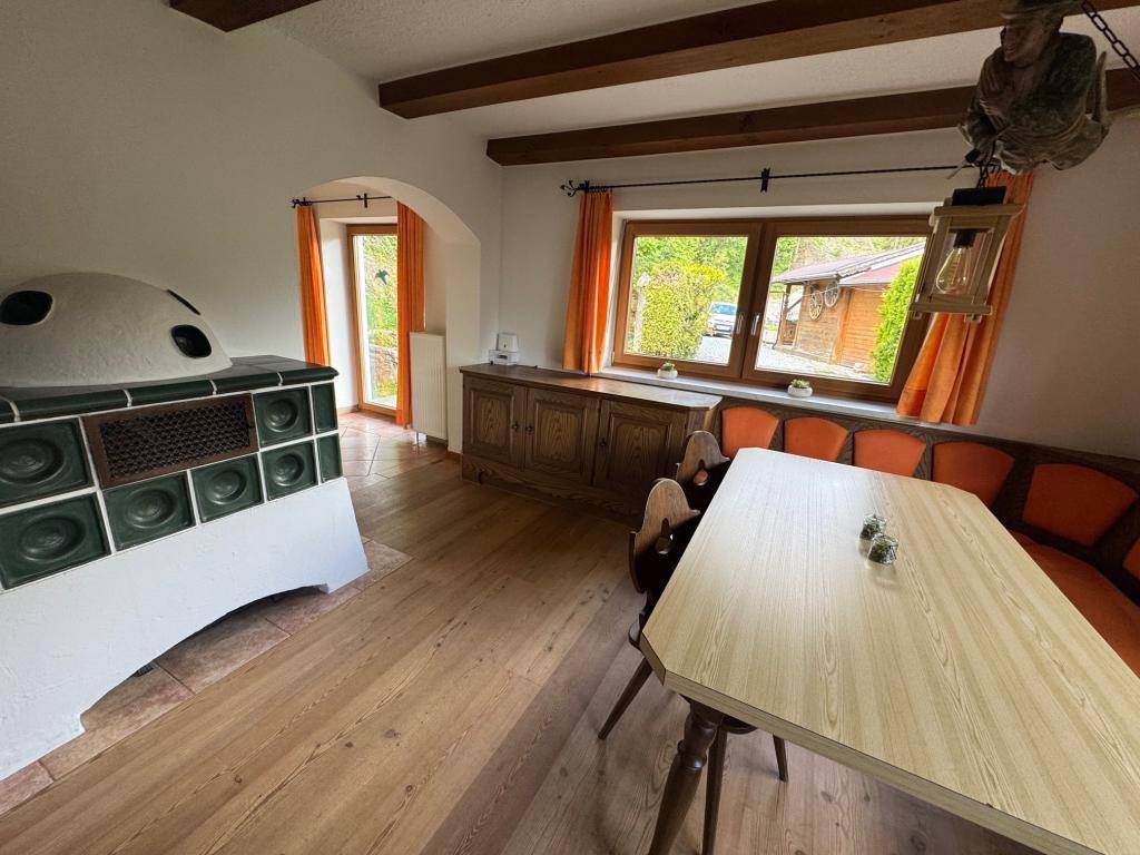 Geräumiger Wohn-Essbereich mit Holzboden, traditionellem Kachelofen und Zugang zum Außenbereich.