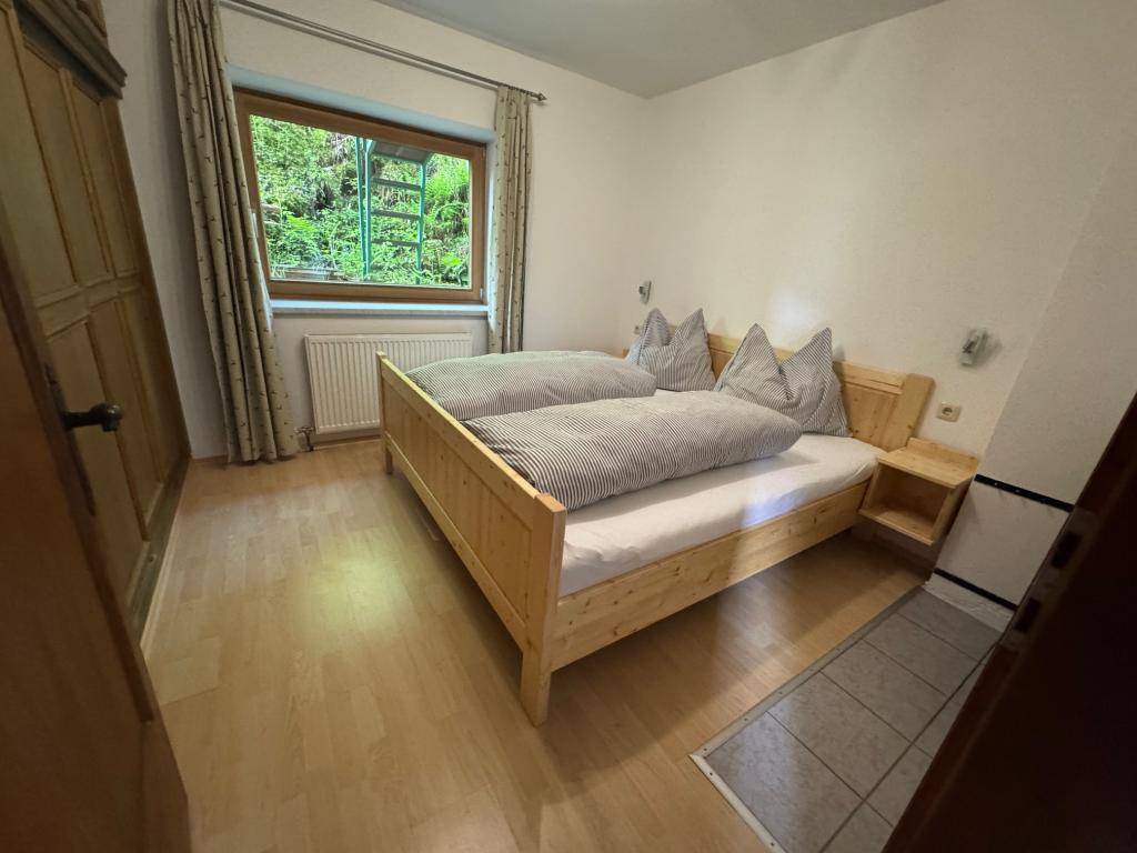 Schlafzimmer mit Doppelbett aus hellem Holz, Holzboden und einem Fenster mit Blick ins Grüne.