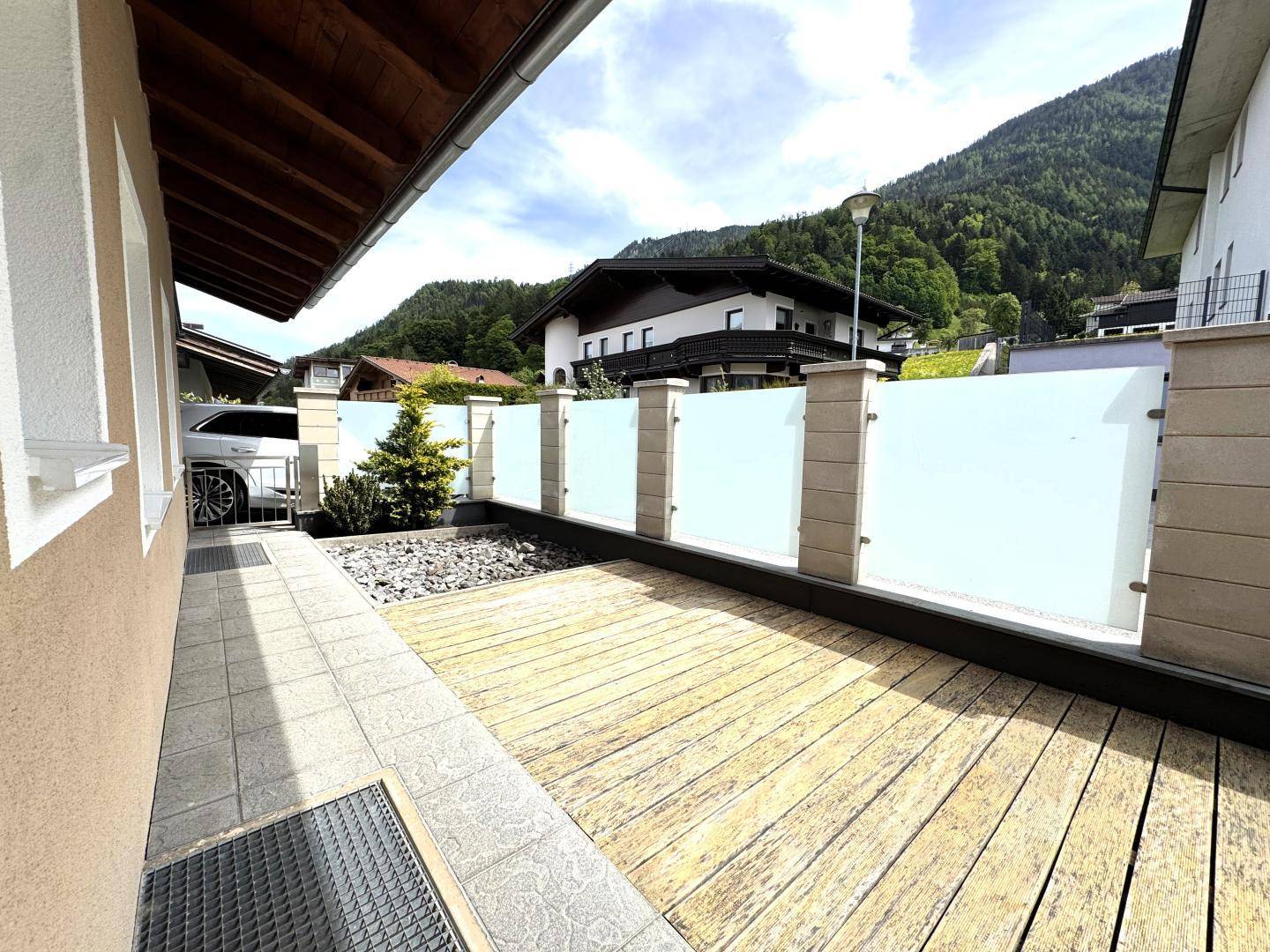 Kleiner Gartenbereich mit Holzterrasse und Kiesbeet, umgeben von einer modernen Glasabtrennung.
