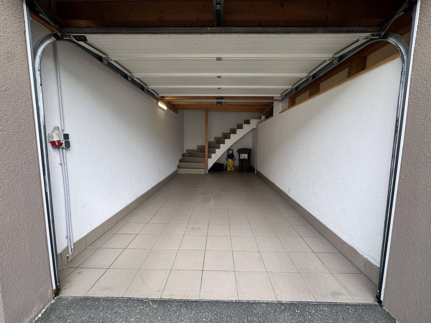 Geräumige Garage mit Fliesenboden und einer Treppe, die zu einem oberen Bereich führt.