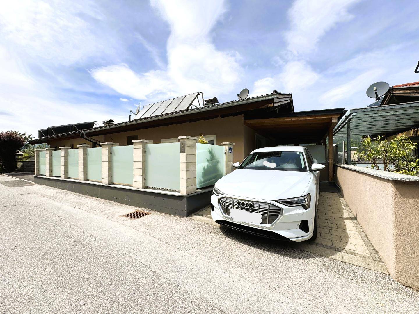 Außenansicht des Hauses mit Carport, Einfahrt und moderner Fassadengestaltung unter blauem Himmel.