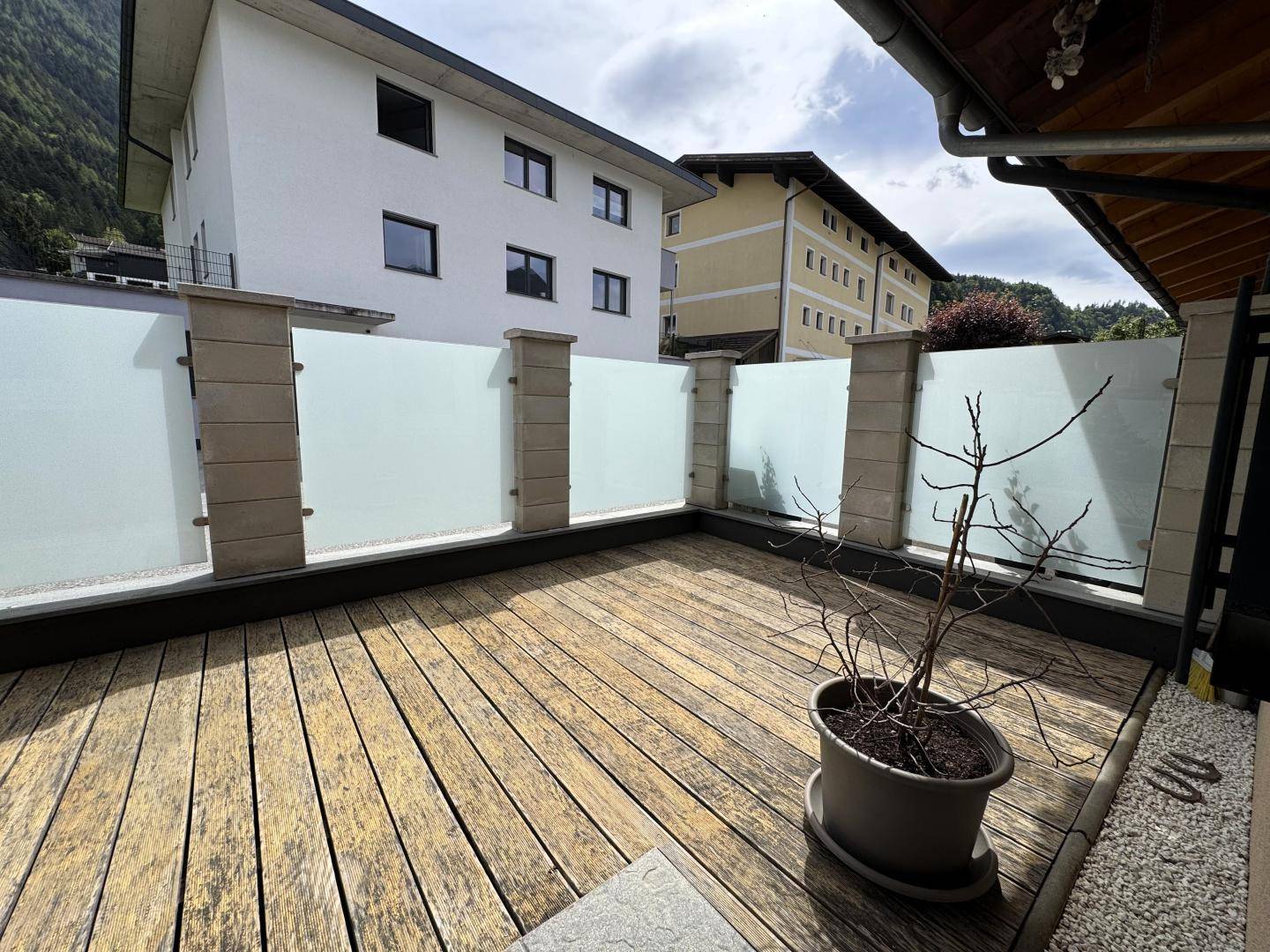 Holzterrasse mit moderner Glasabtrennung und Blick auf die umliegenden Gebäude und Natur.