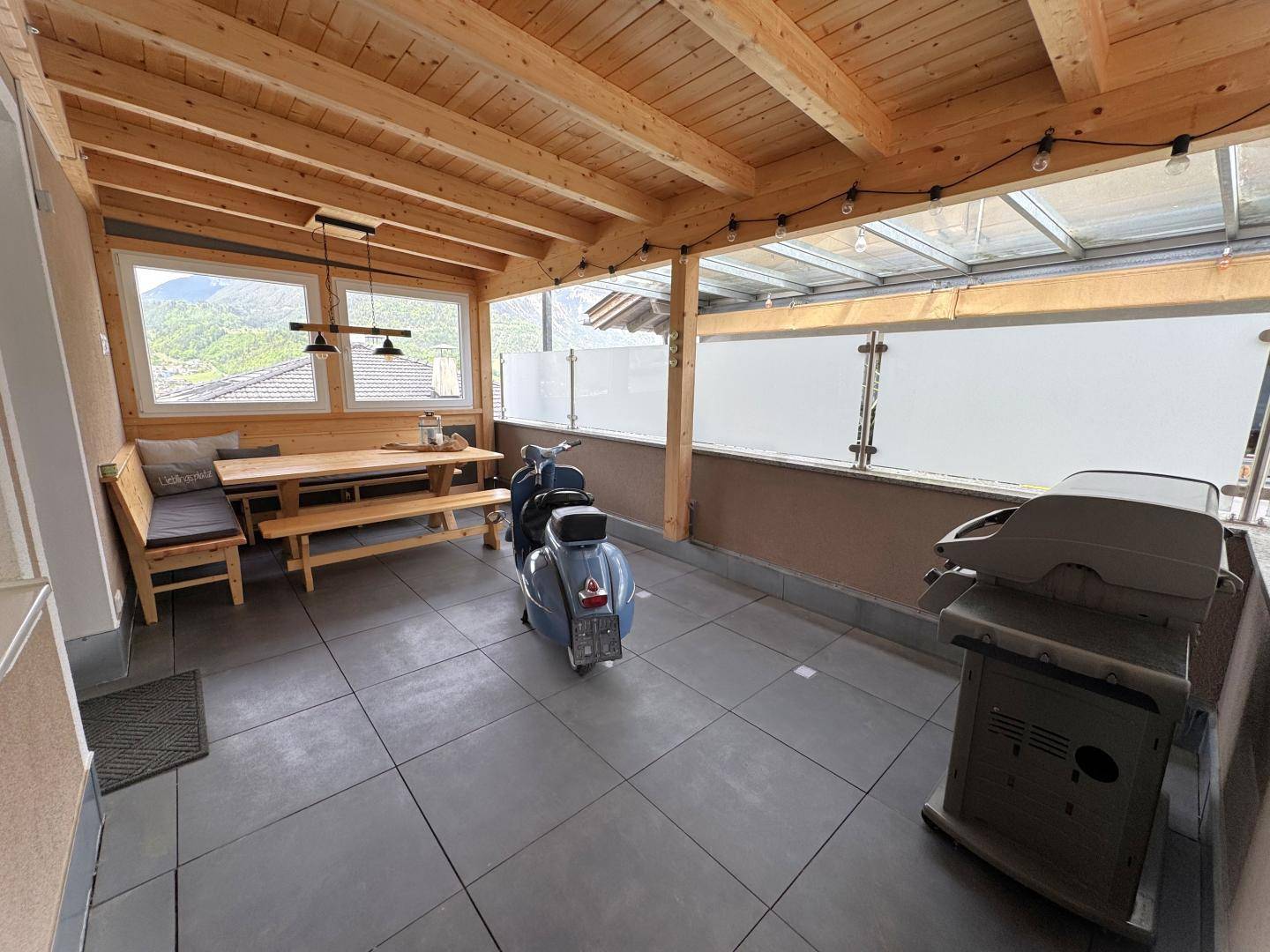 Überdachte Terrasse mit Holzbalken, Essbereich und Grill, ideal für gesellige Stunden im Freien.