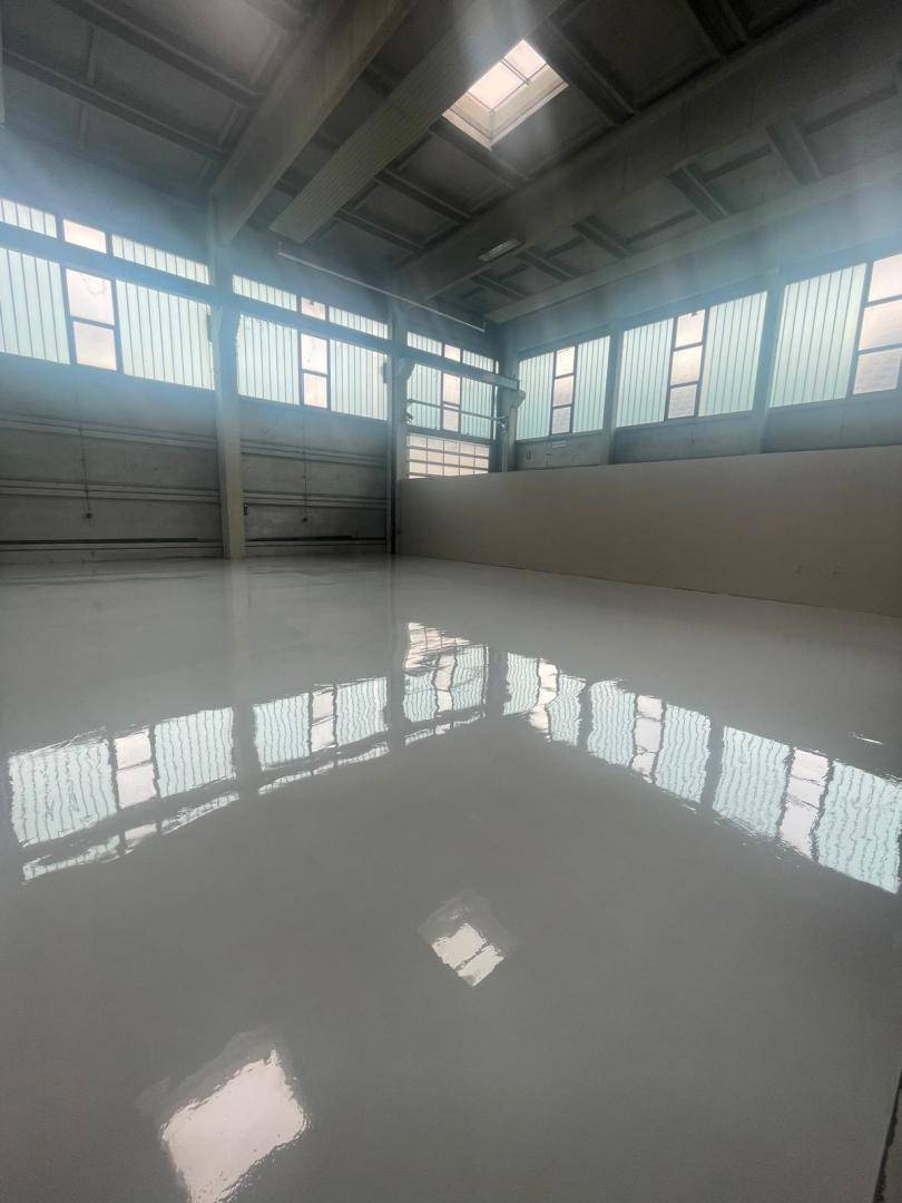 Helle und geräumige Lagerhalle mit reflektierendem Boden, hohen Decken und natürlicher Belichtung durch Fensterreihen.