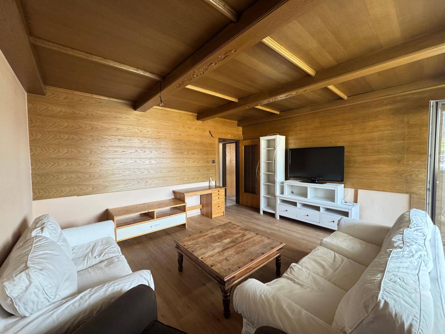 Geräumiges Wohnzimmer mit Holzwänden, Holzbalkendecke und Parkettboden.