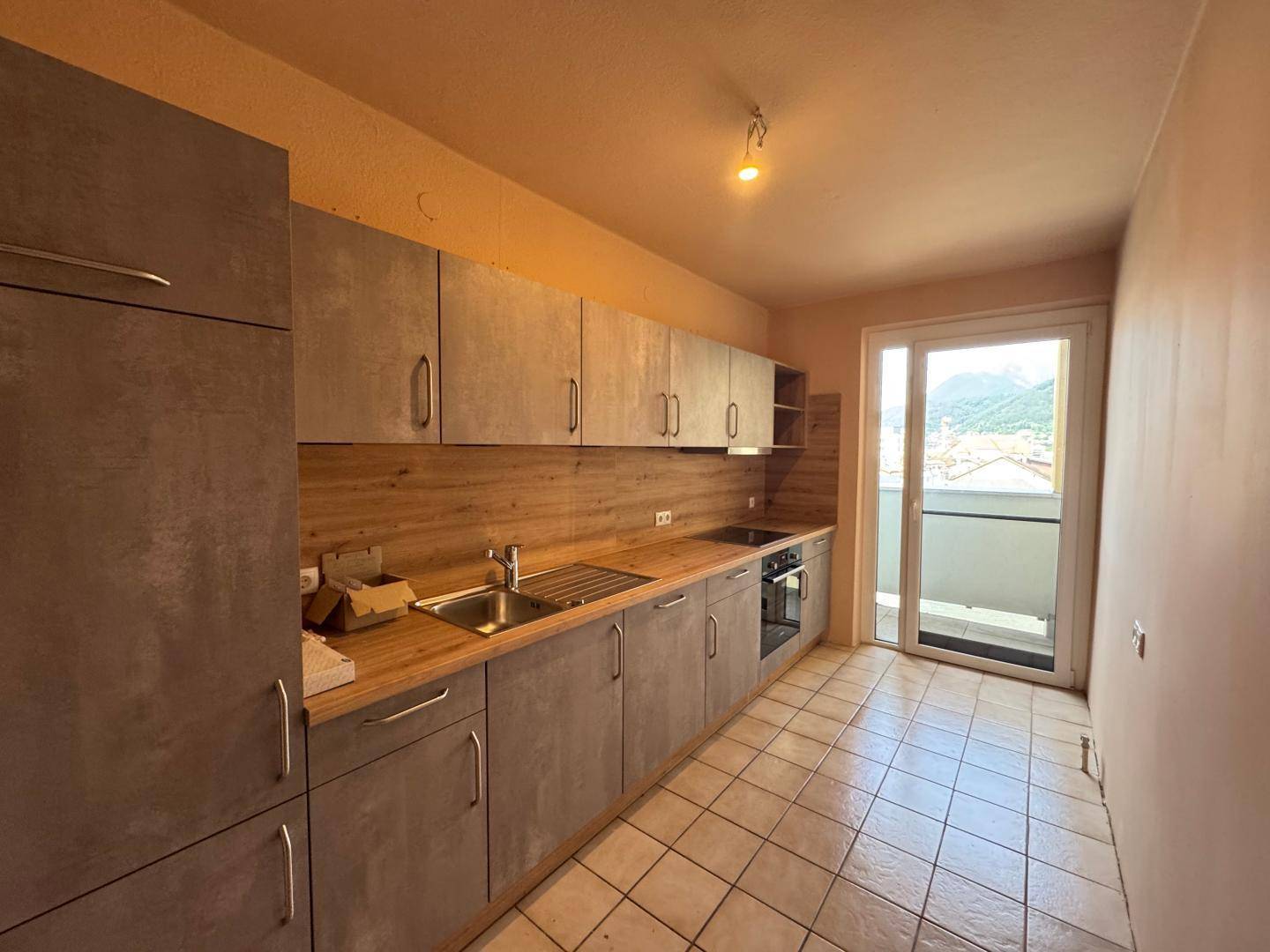 Küche mit grauen Schränken, Holzarbeitsplatte und Zugang zum Balkon.