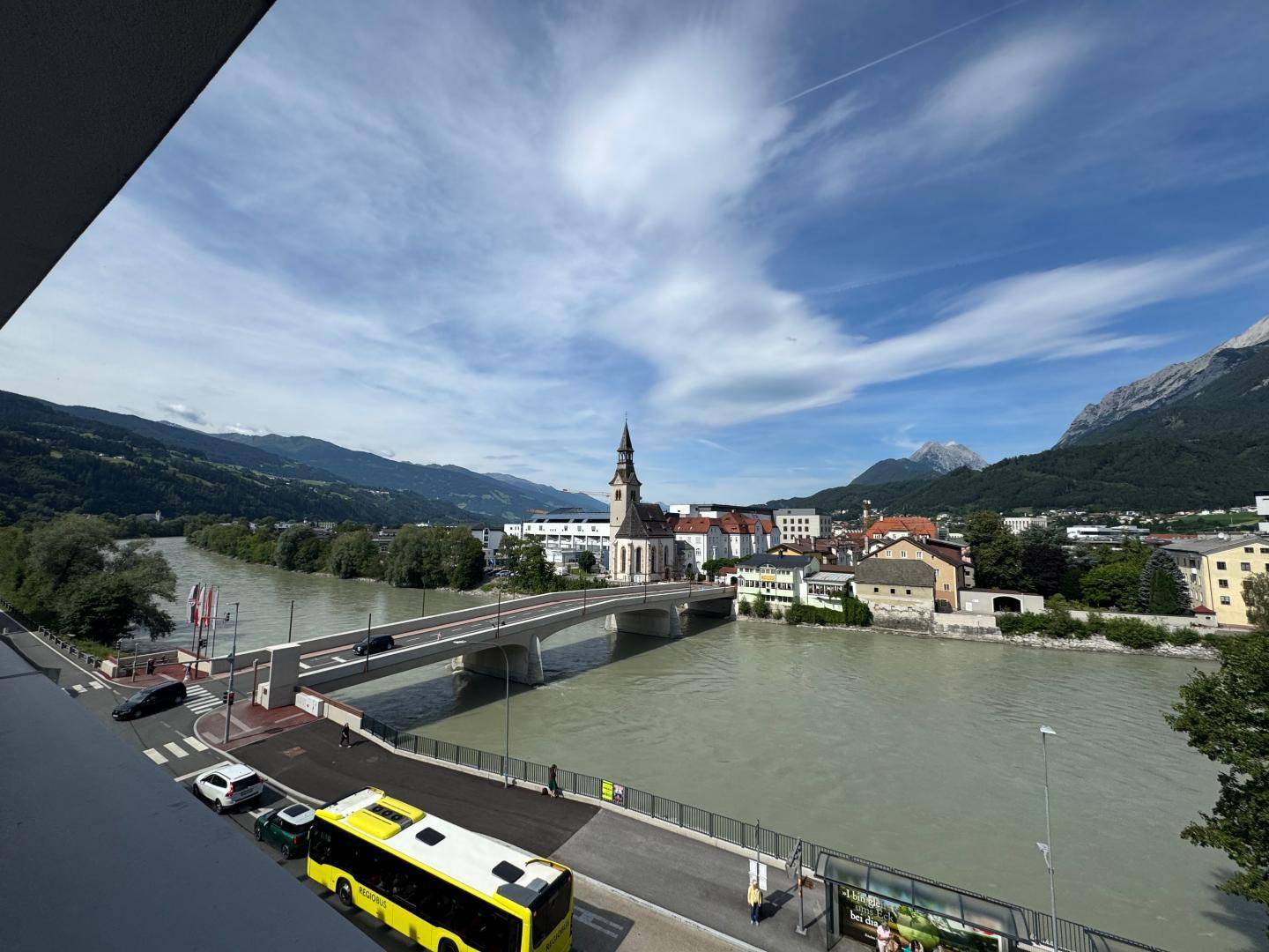 Weitblick über die Stadt mit Fluss, Brücke und beeindruckender Bergkulisse.