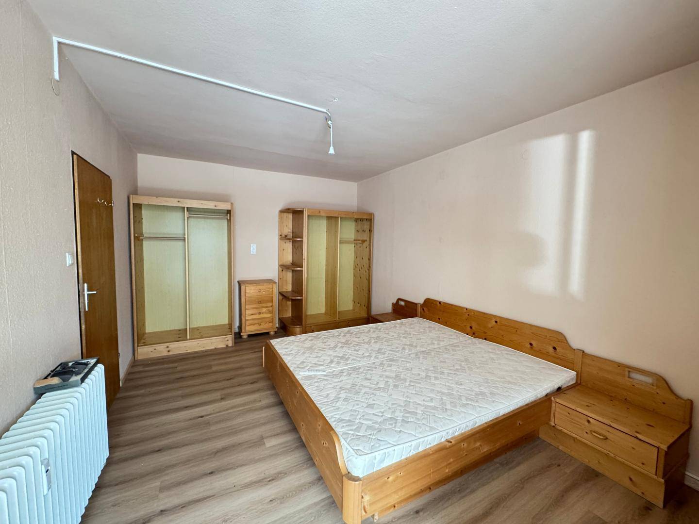 Schlafzimmer mit Doppelbett, Holzschränken und Heizkörper, bereit zur Einrichtung.