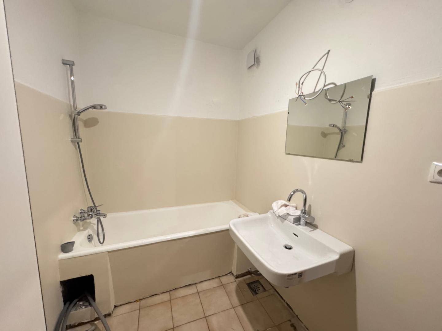 Badezimmer mit Badewanne, Waschbecken und Fliesenboden, renovierungsbedürftig.