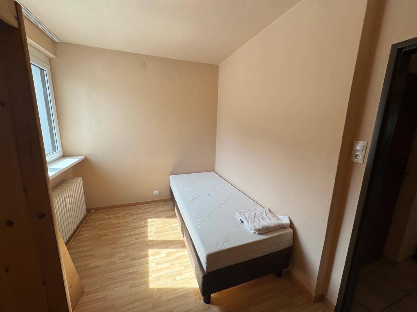 Helles Schlafzimmer mit Einzelbett, Parkettboden und Fenster für Tageslicht.