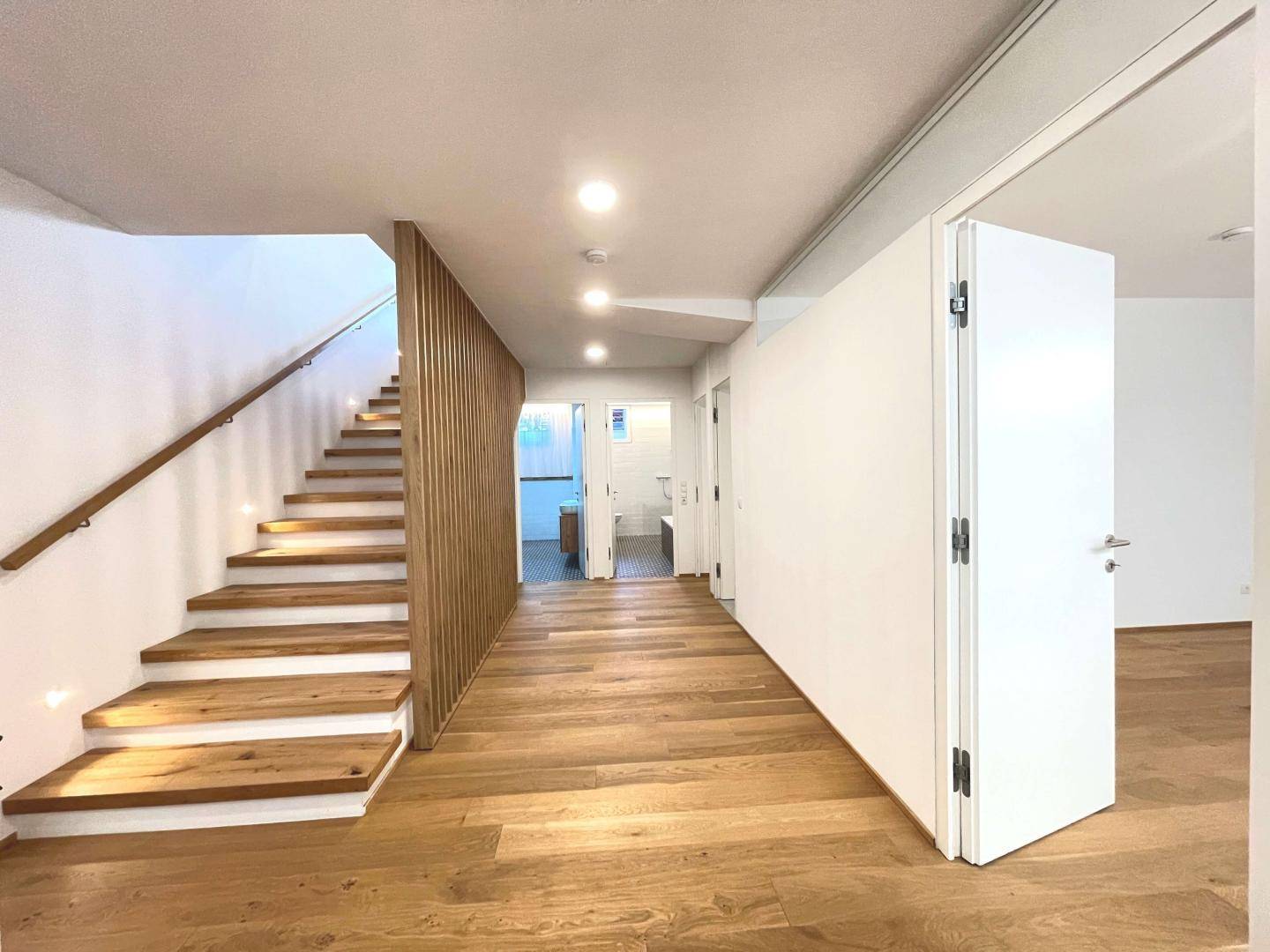 Heller Flur mit Holztreppe, Holzlamellenwand und durchgehendem Parkettboden.