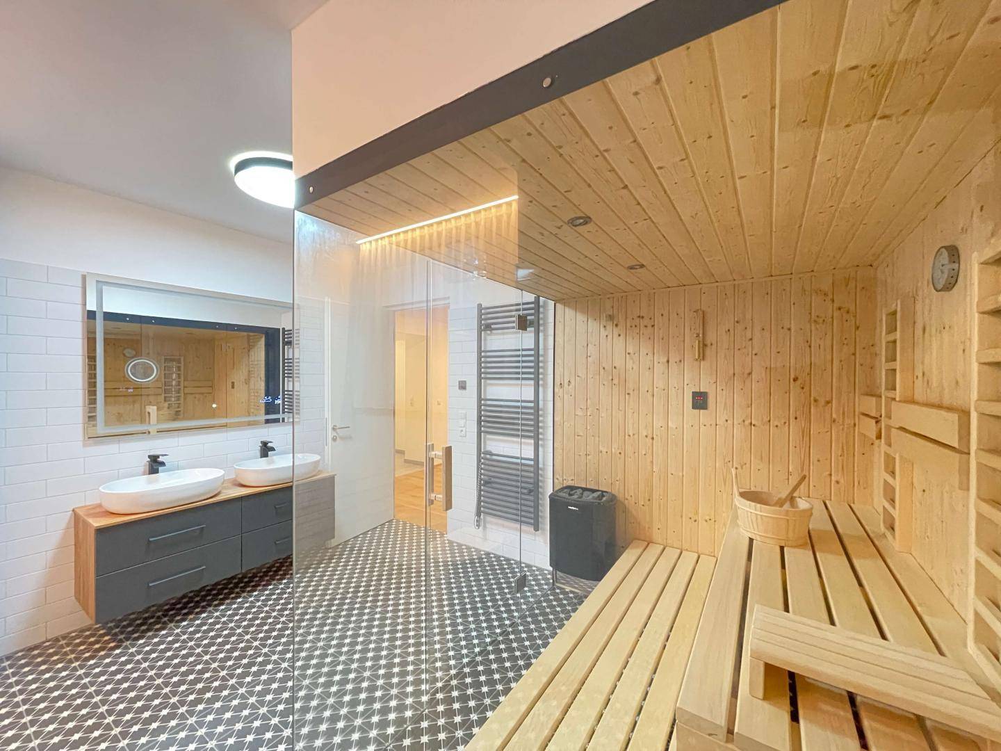 Wellness-Badezimmer mit Sauna, Doppelwaschbecken und stilvollen schwarz-weißen Fliesen.