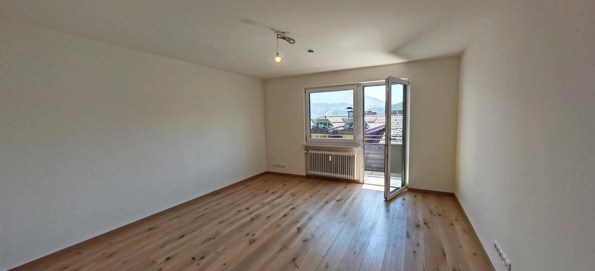 Geräumiger, unmöblierter Wohnbereich mit Holzboden und Zugang zu einem Balkon.