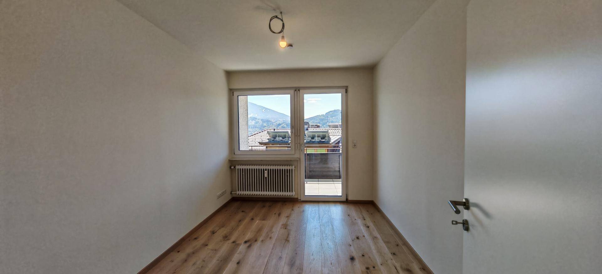Helles, unmöbliertes Schlafzimmer mit Holzboden und Fenster mit Blick auf die Umgebung.