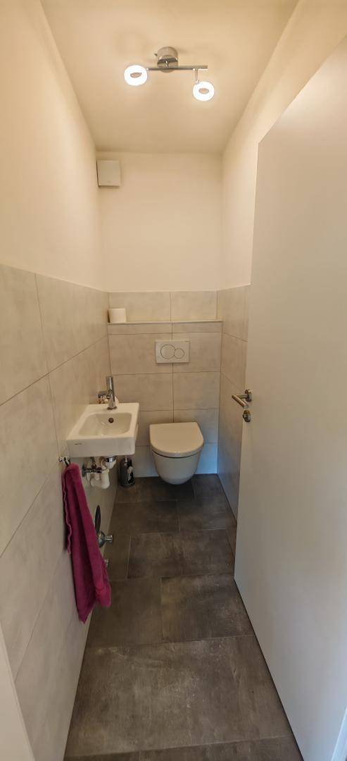 Separate Gästetoilette mit kleinem Waschbecken und Wand-WC in modernem Design.