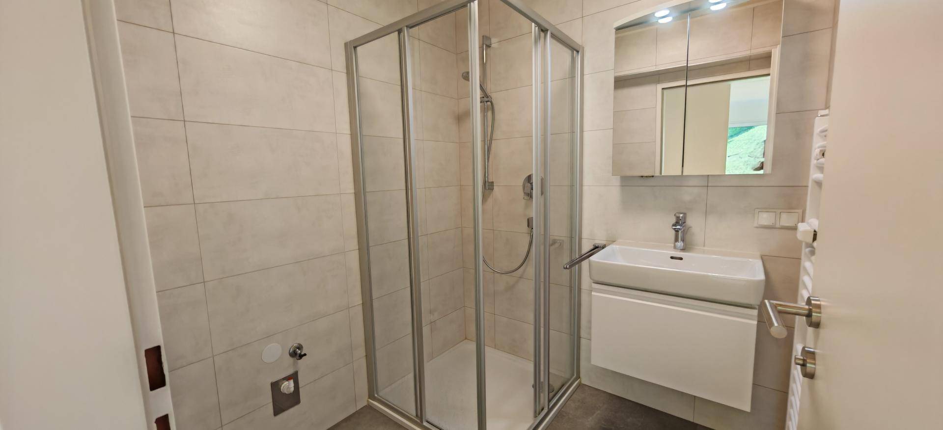 Modernes Badezimmer mit Duschkabine, Waschbecken und Spiegelschrank in hellen Fliesen.