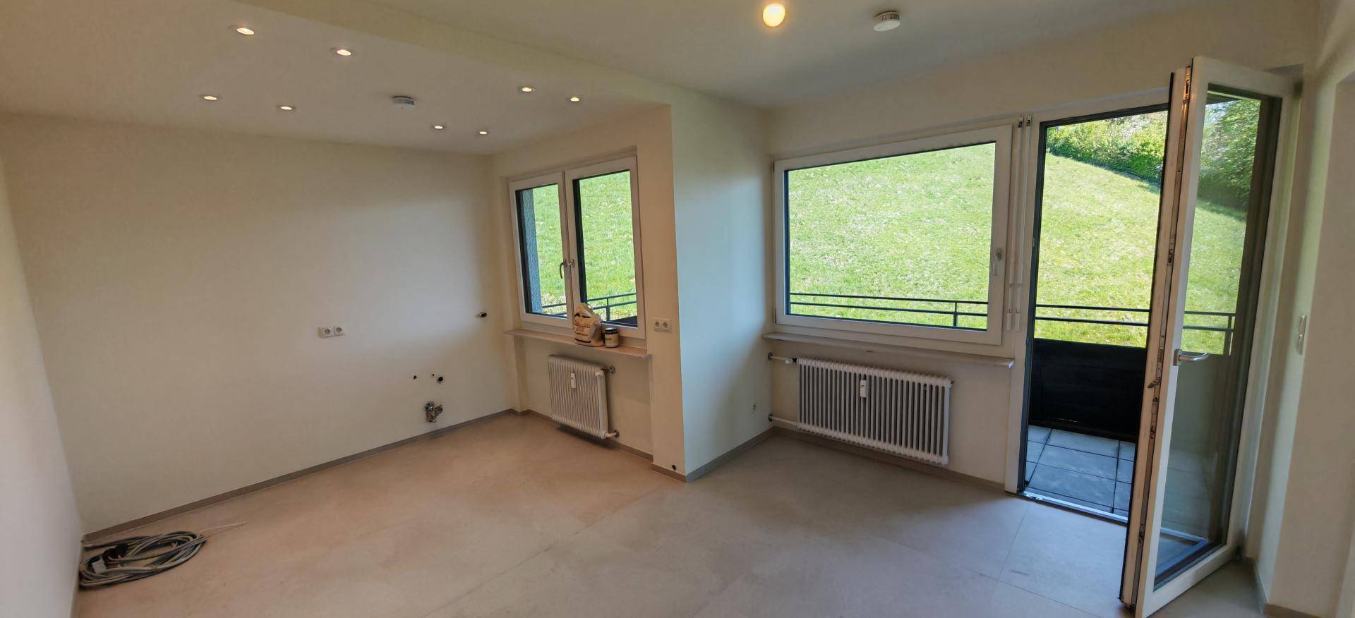Heller, unmöblierter Raum mit Fliesenboden, Heizkörpern und Zugang zu einem Balkon.