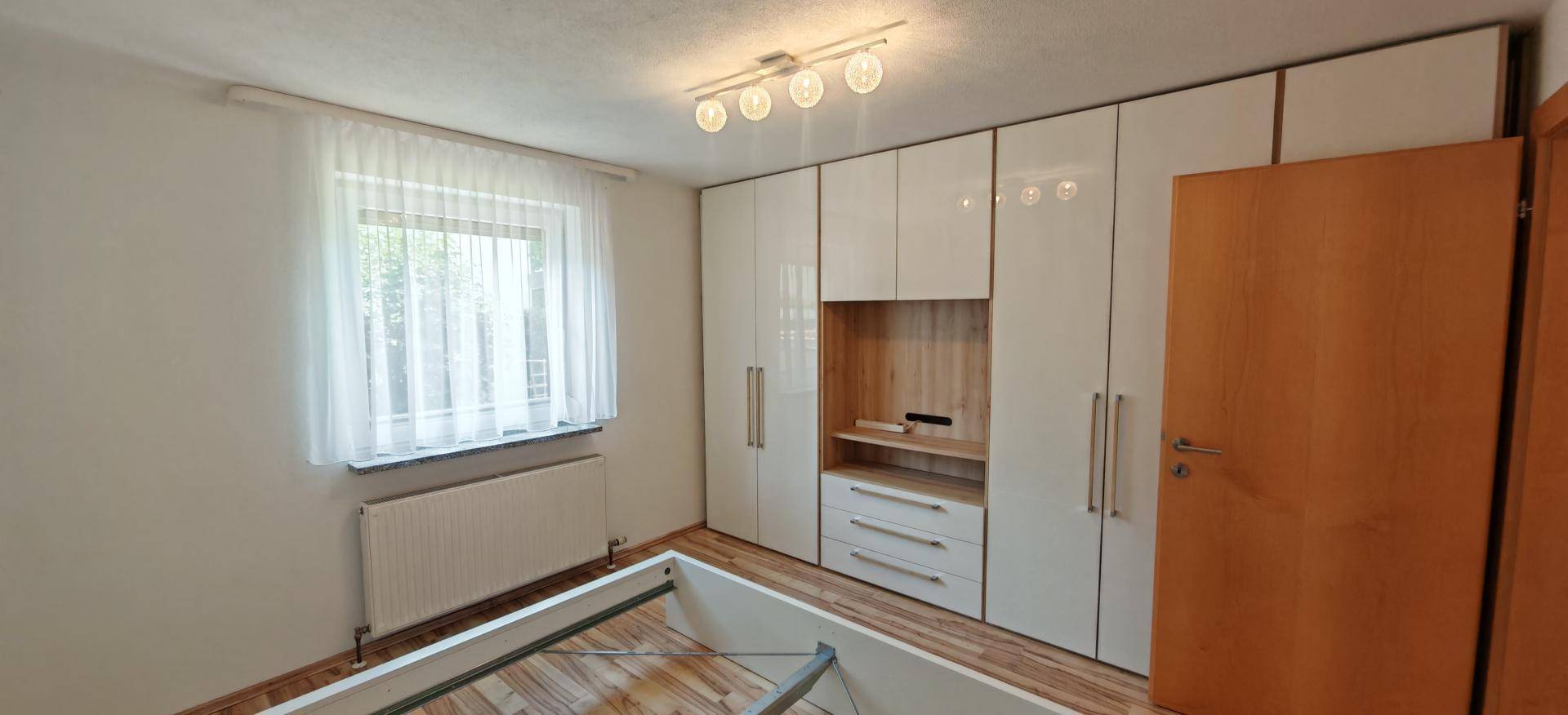 Schlafzimmer mit glänzenden Einbauschränken, Holzboden und Fenster mit Vorhängen.