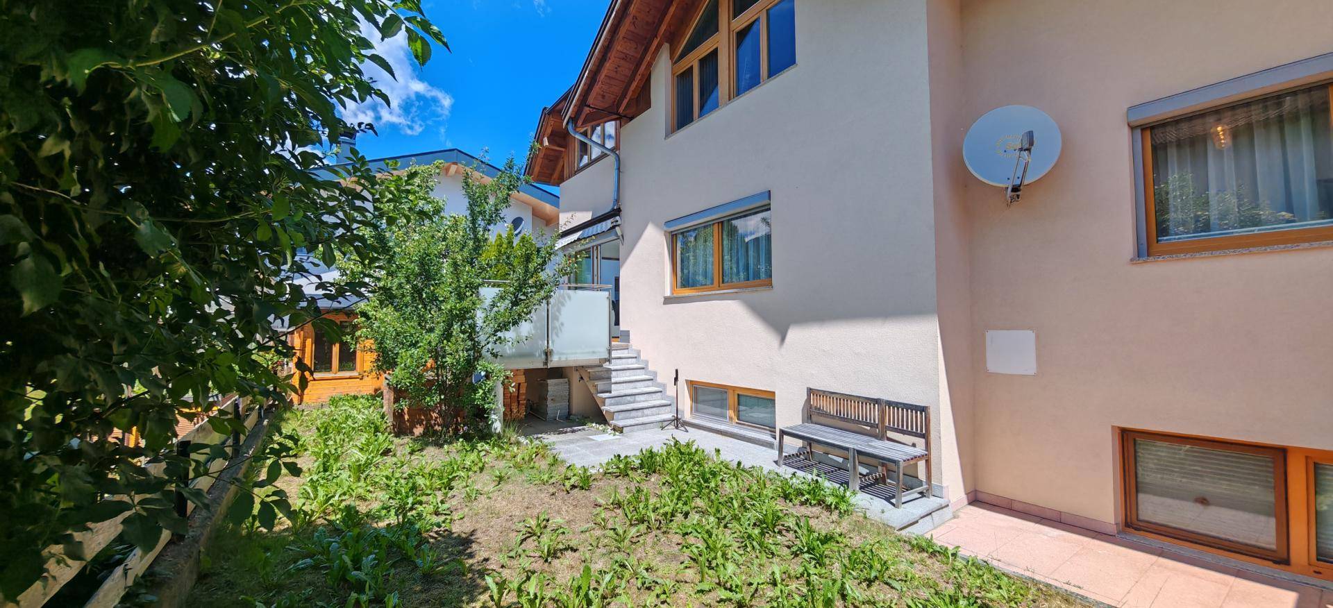 Seitenansicht des Hauses mit kleinem Gartenbereich, Außentreppe und Sitzbank.
