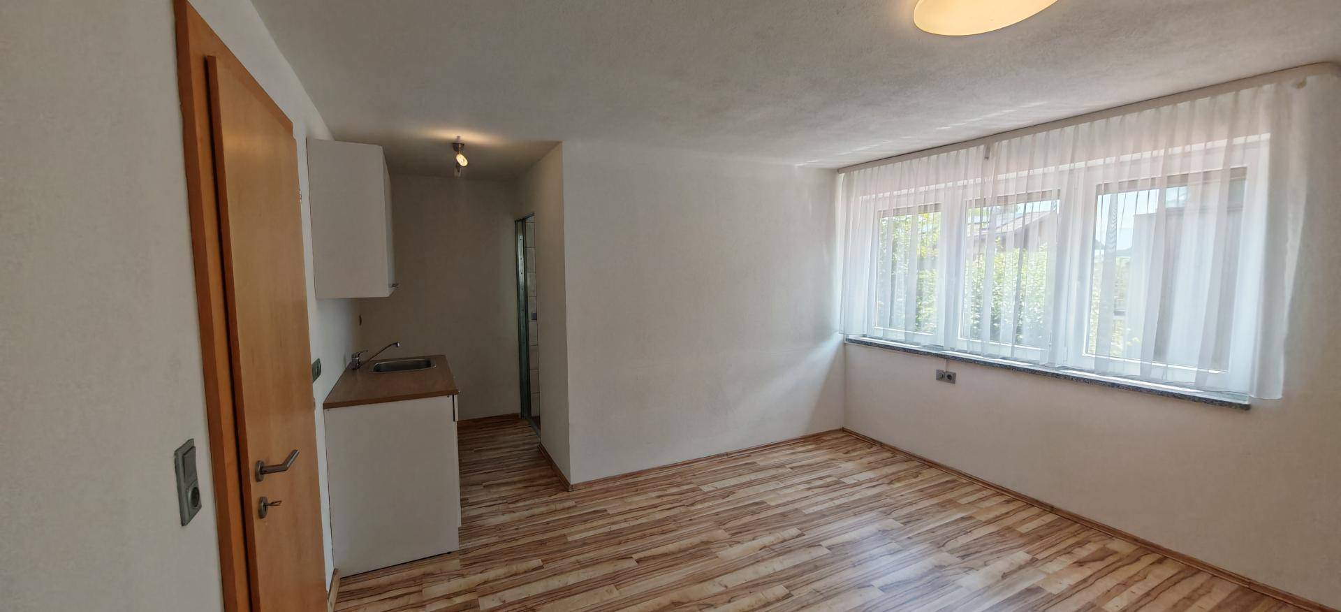 Helles Zimmer mit Holzboden, großen Fenstern und einer praktischen Küchenzeile.