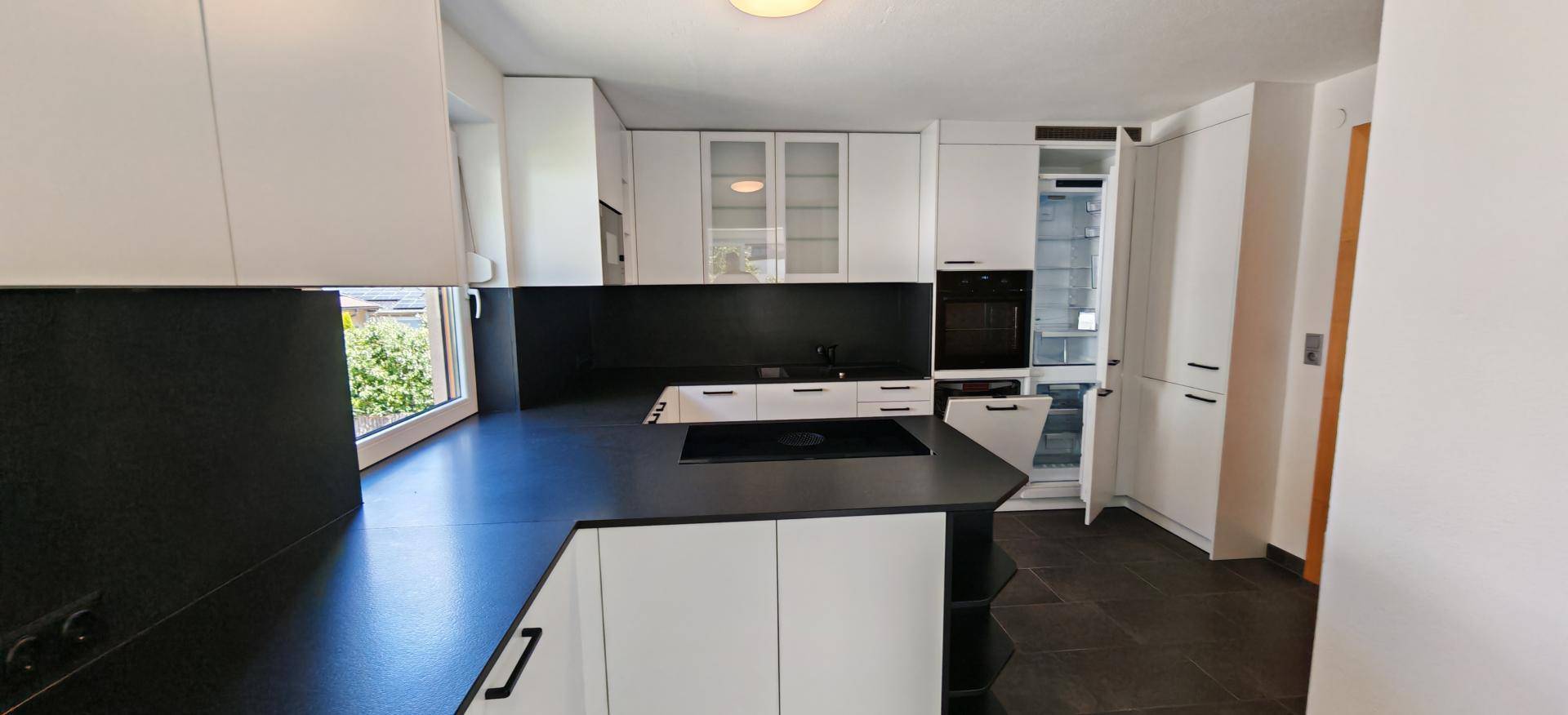 Moderne Einbauküche in Weiß und Schwarz mit integrierten Geräten und dunklem Fliesenboden.