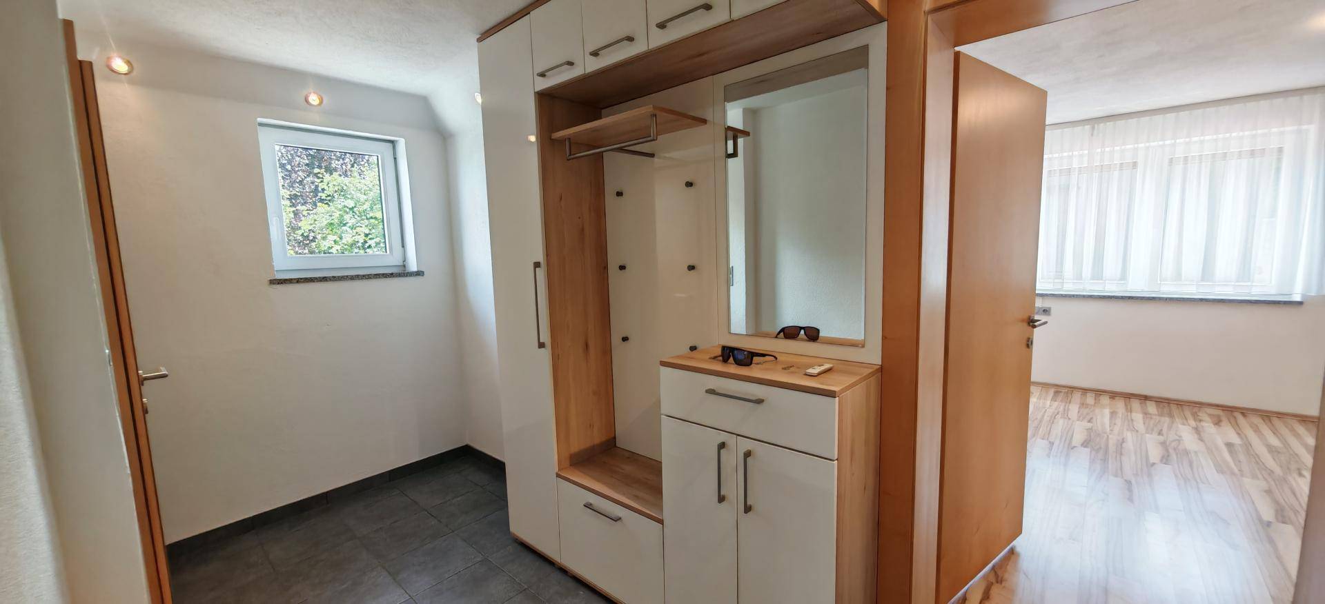 Heller Flur mit Einbauschrank, Spiegel und dunklem Fliesenboden.